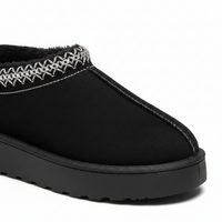 A close-up of a black slip-on mule boot with a thick black platform sole and a decorative white zigzag stitched trim around the collar, set against a plain white background.