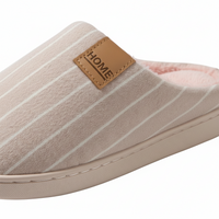 A close-up of a slip-on house slipper with a beige and white striped upper, a tan faux-leather brand patch reading 'HOME', and a light pink fleece lining visible at the opening.