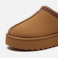 A close-up of a brown slip-on clog-style boot with a thick lug sole and a patterned knit trim visible at the opening, photographed on a clean white background.