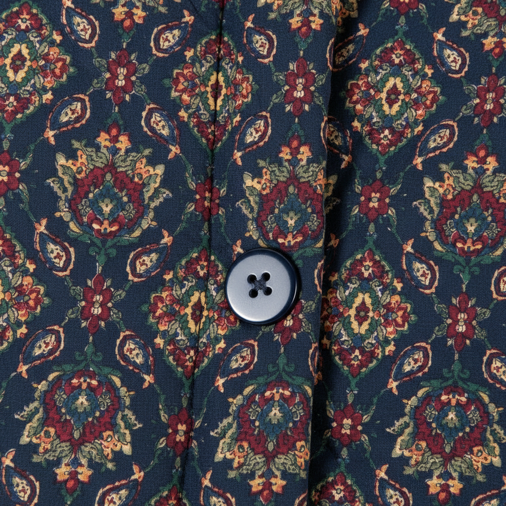 Close-up of a button-front garment with a dark navy base and an ornate floral paisley pattern in red, green, and beige, featuring a single four-button snap closure.