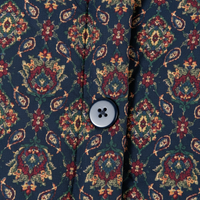 Close-up of a button-front garment with a dark navy base and an ornate floral paisley pattern in red, green, and beige, featuring a single four-button snap closure.