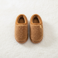 A pair of tan sherpa fleece slipper shoes with brown soles, photographed from a top-down view on a white textured background.