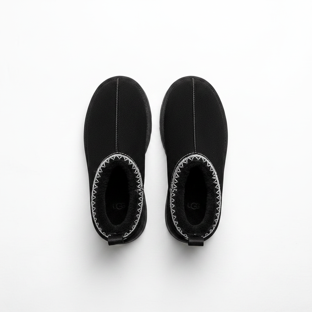 A pair of black UGG slip-on ankle boots with white contrast stitching around the collar, shown from a top-down view on a white background.