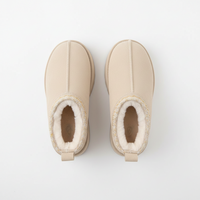 A pair of beige slip-on winter boots with white shearling lining and a decorative gold glitter trim around the collar, shown from a top-down view on a white background.