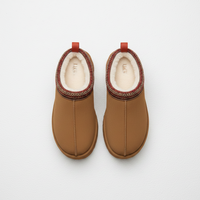 A pair of UGG slip-on ankle boots in tan brown, featuring a cream shearling lining, a patterned trim around the collar, and red pull tabs at the top, shown from a top-down view on a white background.