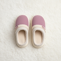 A pair of slip-on indoor slippers with ribbed mauve-pink uppers, cream ribbed trim, and cream interiors, photographed from above on a soft white textured rug.