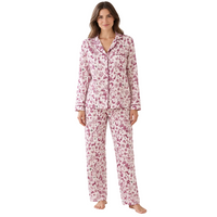 A woman stands in a bright living room wearing a matching pajama set with a pink and white floral print. The set includes a long-sleeve button-up top and coordinating pants.