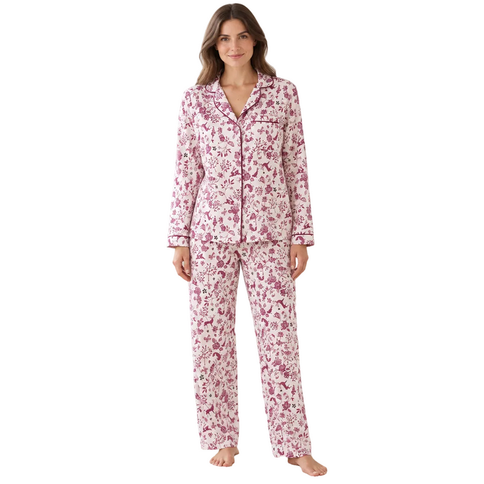 A woman stands in a bright living room wearing a matching pajama set with a pink and white floral print. The set includes a long-sleeve button-up top and coordinating pants.