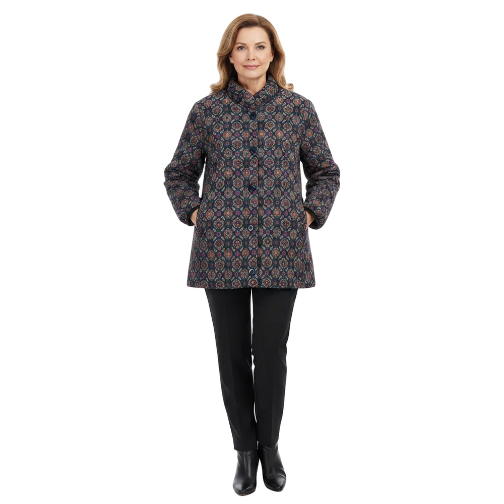 A woman modeling a mid-length quilted coat with a geometric pattern in navy, red, and beige, paired with black pants and black ankle boots, on a solid white background.