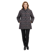 A woman modeling a mid-length quilted coat with a geometric pattern in navy, red, and beige, paired with black pants and black ankle boots, on a solid white background.