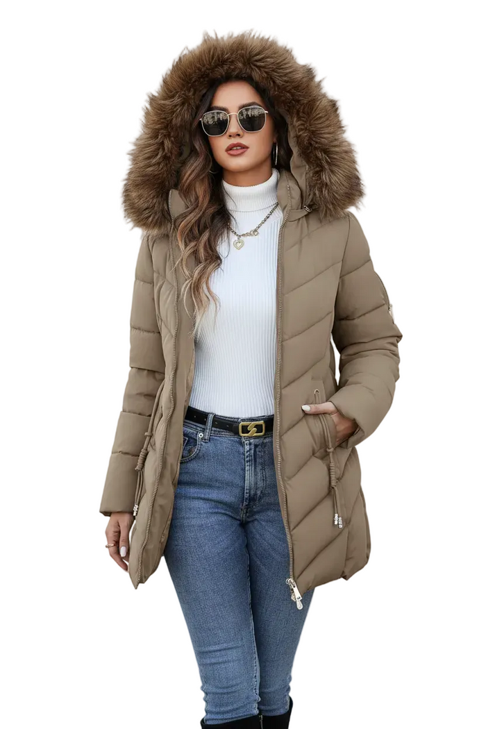 A woman modeling a mid-length taupe-brown puffer coat with a large brown faux-fur trimmed hood, worn over a white ribbed turtleneck and blue jeans, against a plain white background.