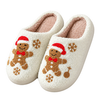 A pair of fluffy white sherpa slip-on slippers decorated with brown gingerbread men wearing red Santa hats, red bow ties, and brown snowflakes, shown on a clean white background.
