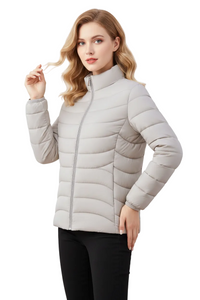 A woman modeling a light beige puffer jacket with a stand-up collar and front zipper, paired with black pants, against a plain white background.