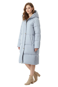 A woman modeling a long, light blue hooded puffer coat with gold-tone buttons, paired with beige ankle boots, against a plain white studio background.