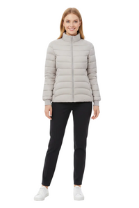 A woman modeling a light gray puffer jacket with a high collar and front zipper, paired with black pants and white sneakers, against a plain white background.