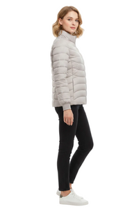 A woman modeling a light gray puffer jacket, paired with black skinny jeans and white sneakers, shown from a side profile against a plain white studio background.