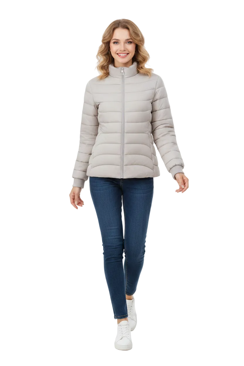 A woman modeling a light gray puffer jacket with a stand-up collar and front zipper, paired with dark blue skinny jeans and white sneakers, against a plain white studio background.