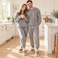 A man and a woman standing in a bright, modern kitchen, both wearing matching gray fuzzy long-sleeve sweaters and jogger pants with gray slip-on slippers.