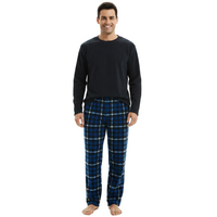 A man modeling a two-piece pajama set consisting of a solid black long-sleeve crewneck shirt and blue plaid pajama pants with white and black lines, shot against a solid white background.