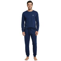 A man modeling a navy blue long-sleeve pajama set with a small white embroidered logo on the left chest, paired with matching navy jogger pants, against a plain white background.