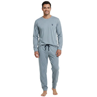 A man modeling a light blue-gray long-sleeve pajama top and matching jogger pants with a dark drawstring, standing against a plain white background.
