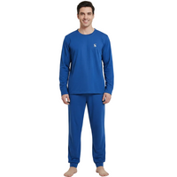 A man modeling a royal blue long-sleeve pajama set with a small white embroidered logo on the left chest, paired with matching blue pants, against a light gray studio background.