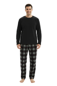 A man modeling a two-piece pajama set consisting of a solid black long-sleeve shirt and black, white, and gray plaid pants, standing against a plain white background.