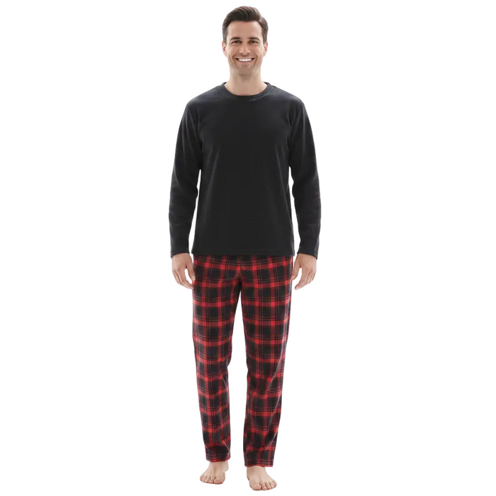 A man standing against a plain white background wearing a black long-sleeve crewneck shirt and red and black plaid pajama pants.
