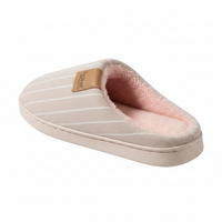 A single slip-on mule house slipper shown from a three-quarters angle on a white background. The slipper features a light beige fabric upper with thin white stripes, a soft pink fleece lining, and a tan faux-leather brand patch on the side.