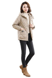 A woman modeling a light beige quilted puffer jacket with a hood, worn over a cream turtleneck, black skinny jeans, and tan ankle boots, against a plain white background.