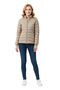 A woman modeling a light beige quilted puffer jacket with a high collar and front zipper, paired with dark blue skinny jeans and white sneakers, against a plain white studio background.