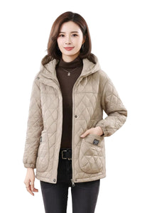 A woman modeling a light beige quilted hooded jacket over a dark brown turtleneck sweater and black pants, set against a plain white background.