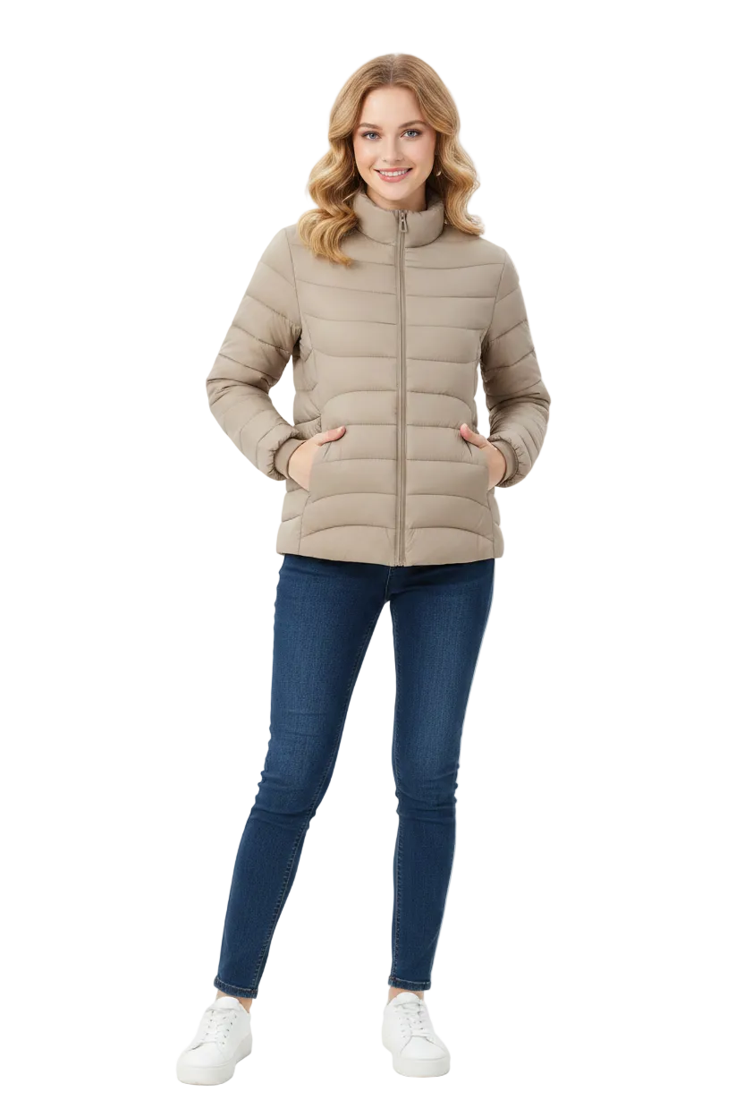 A woman modeling a light beige puffer jacket with a high collar and front zipper, paired with dark blue skinny jeans and white sneakers, against a plain white studio background.