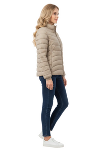 A woman modeling a light beige puffer jacket, paired with dark blue skinny jeans and white sneakers, shown in a side profile against a plain white studio background.