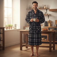 A man stands barefoot in a bright kitchen wearing a dark navy and white plaid bathrobe and holding a white mug.
