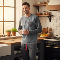 A man wearing a gray and white striped long-sleeve henley pajama shirt with matching gray pants stands in a bright, modern kitchen holding a white mug.