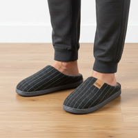 A person wearing dark charcoal gray pinstriped slippers with a small tan brand patch reading 'SOUVENIR', paired with dark jogger pants on a light wood floor.