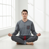 A man sits cross-legged in a bright, minimalist room wearing a gray long-sleeve striped henley shirt with a chest pocket and matching gray pants with a red drawstring.