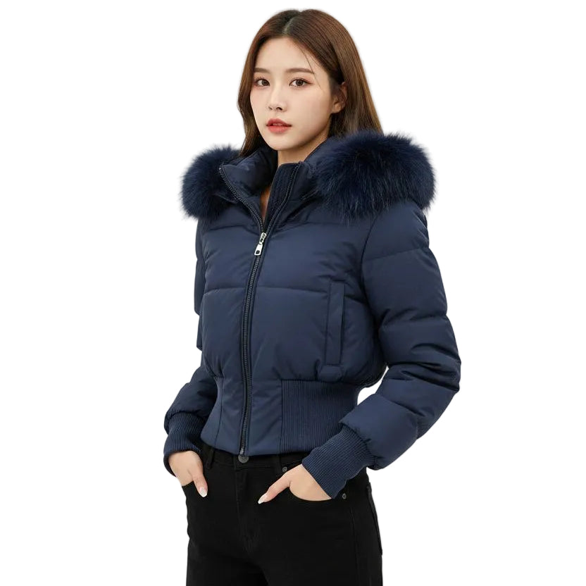 A woman wearing a navy blue puffer jacket with a large dark fur-trimmed hood, paired with black pants, against a light gray studio background.