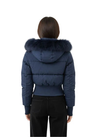 A model viewed from the back wearing a navy blue puffer jacket with a large dark fur-trimmed hood and black pants, set against a plain light gray studio background.