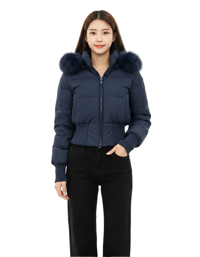 A woman modeling a navy blue cropped puffer jacket with a fluffy dark fur-trimmed hood, paired with black pants, against a solid white background.