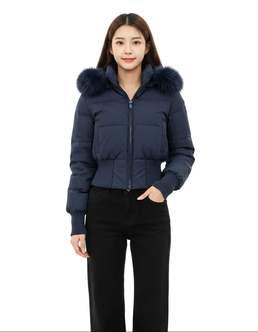 A woman modeling a navy blue cropped puffer jacket with a fluffy dark fur-trimmed hood, paired with black pants, against a solid white background.
