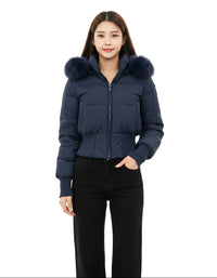 A woman modeling a navy blue cropped puffer jacket with a fluffy dark fur-trimmed hood, paired with black pants, against a solid white background.