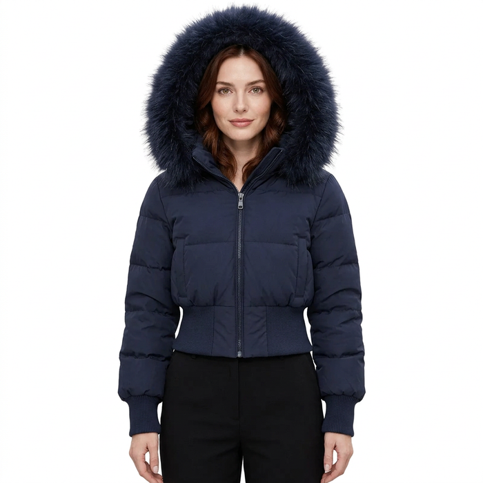 A woman wearing a cropped navy blue puffer jacket with a large dark navy faux-fur trimmed hood, paired with black pants, against a plain white background.