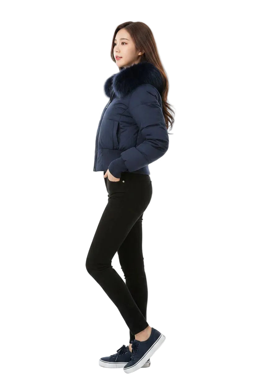 A woman modeling a navy blue puffer jacket with a large dark fur collar, paired with black skinny pants and navy sneakers, against a plain white background.