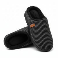 A pair of slip-on indoor slippers with a black and white pinstripe pattern, black plush fleece lining, and a small brown leather brand tag that reads HOME.