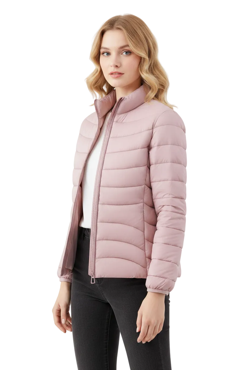 A woman modeling a light pink puffer jacket with a stand-up collar and front zipper, worn over a white top and black pants against a plain light gray studio background.