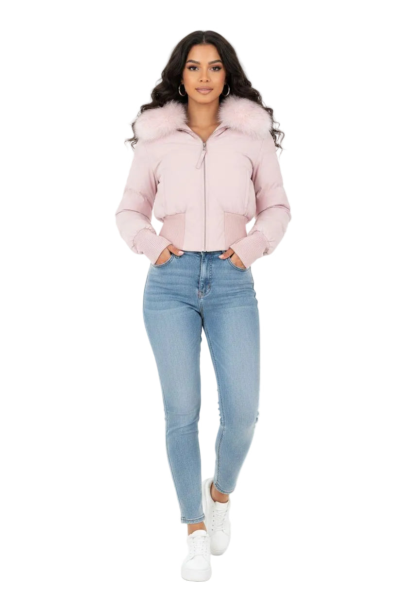 A woman modeling a light pink cropped puffer jacket with a fluffy faux-fur collar, paired with light blue skinny jeans and white sneakers, against a solid white background.