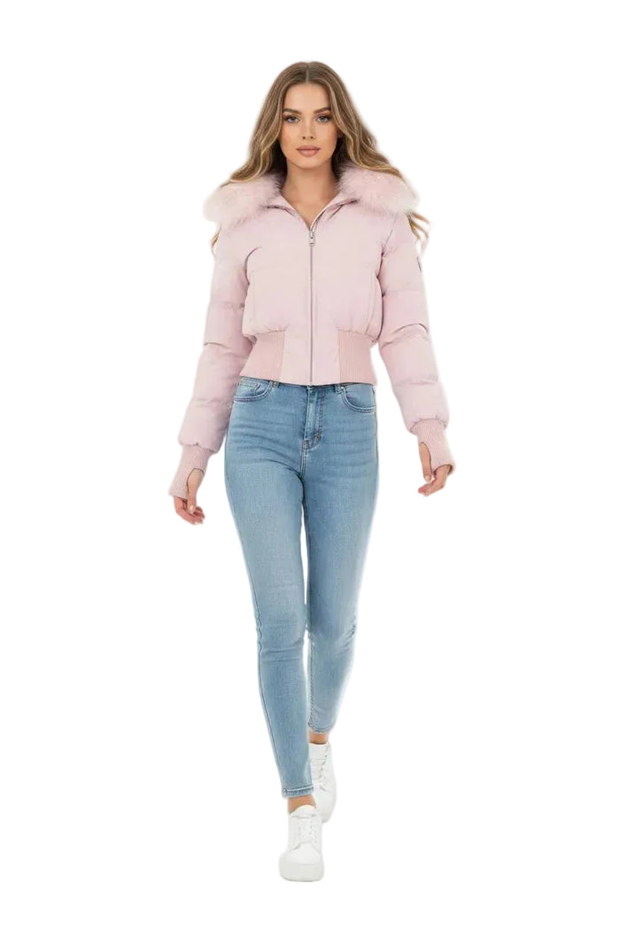 A woman modeling a light pink cropped puffer jacket with a fluffy faux-fur collar, paired with light-wash blue skinny jeans and white sneakers, against a solid white studio background.