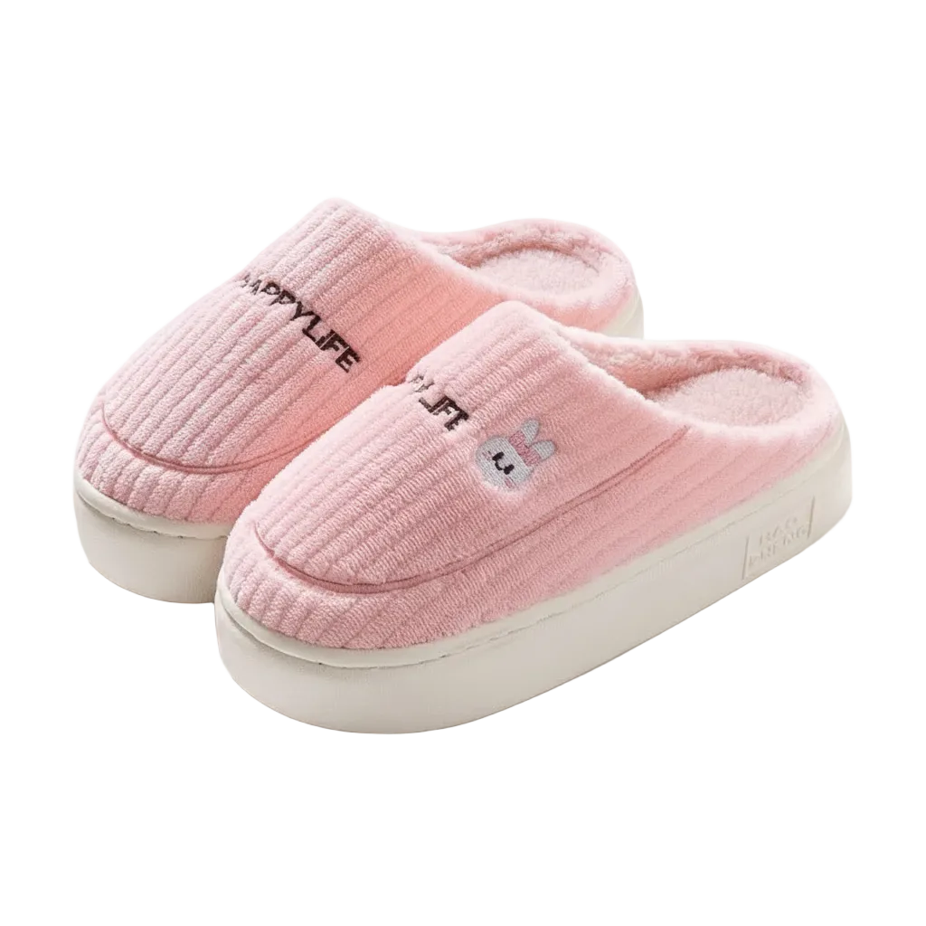 A pair of pink ribbed fleece slip-on slippers with white soles. One slipper features the text 'HAPPYLIFE' in black, and the other has a small embroidered bunny face.
